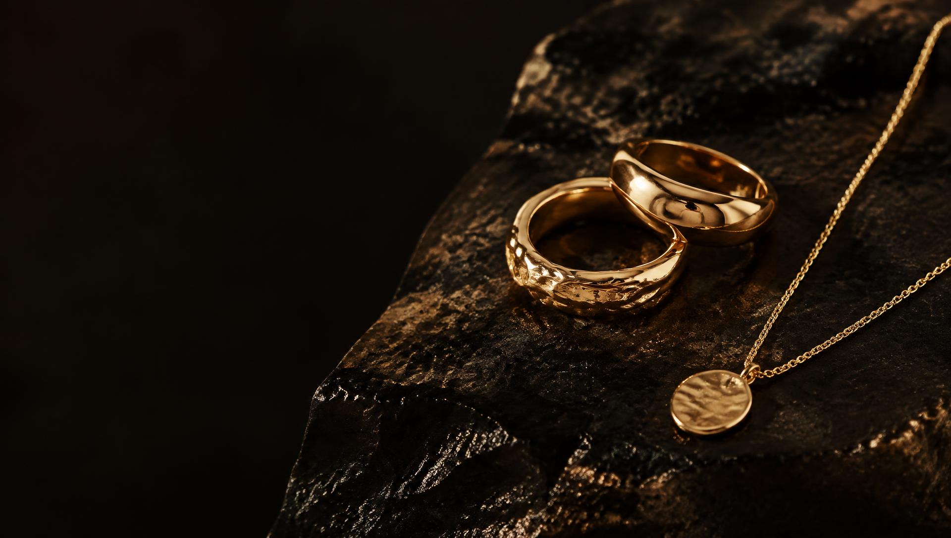 Gold vermeil rings and pendant resting on dark stone